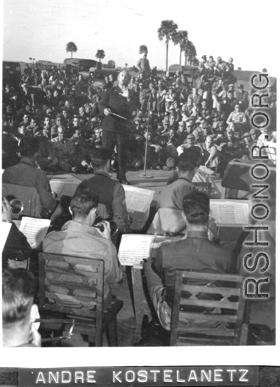 Conductor Andre Kostelanetz directs at a USO show in Gushkara, India, during WWII.  The boxes in front of the band players are labeled 748th ROB (748th Railway Operating Battalion).