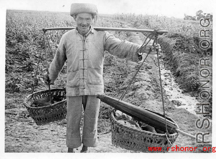 A farmer in Yunnan province carries items in baskets on a shoulder pole. During WWII.