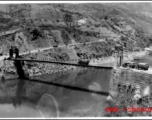 Trucks wait to cross a bridge on the Salween River one at a time. Note how the bridge bends down under the load of the transport truck going across. During WWII.