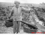 A farmer in Yunnan province carries items in baskets on a shoulder pole. During WWII.